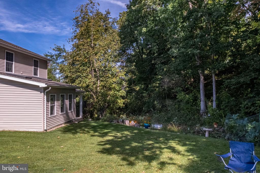 House beside a broad lawn and wooded backyard, with a small garden and blue folding chair.