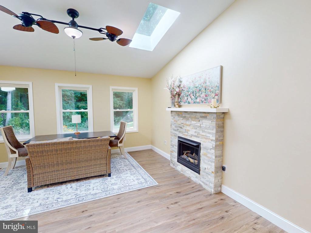 Dining area with wicker furniture, stone fireplace, three garden-facing windows, and a skylight.