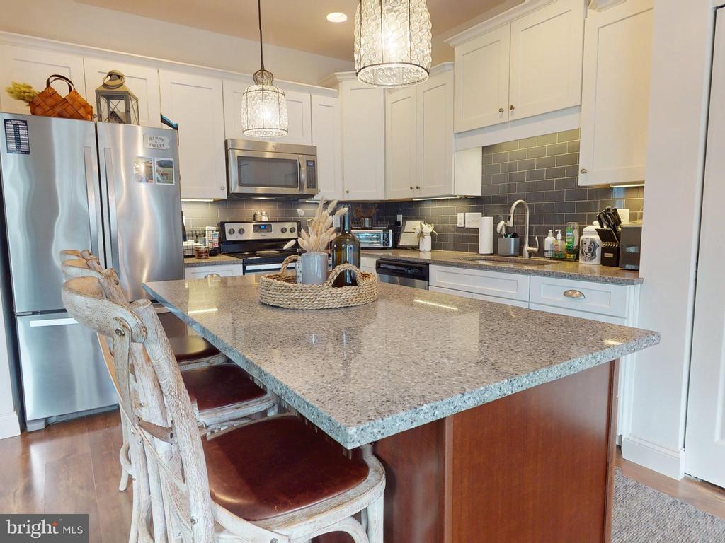 Kitchen with a large granite island, white cabinets, stainless steel appliances, and dark tile backsplash.