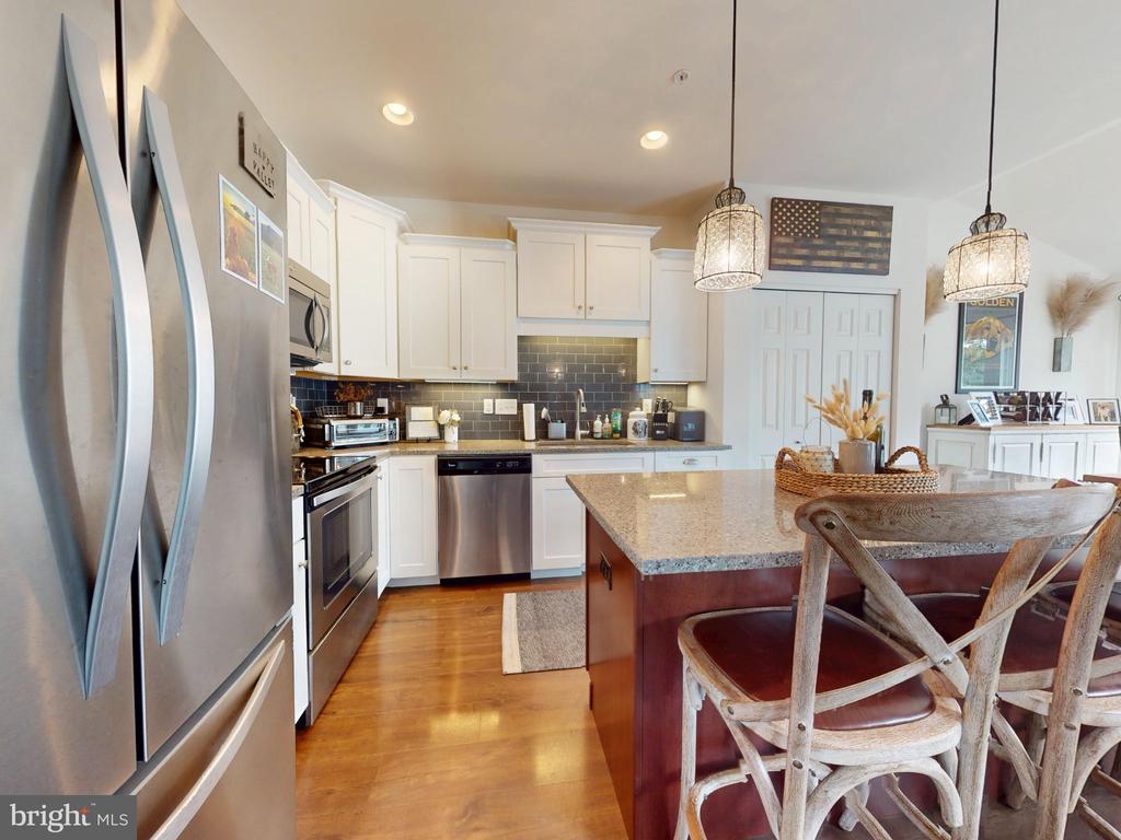 Kitchen with white cabinets, stainless steel appliances, dark tile backsplash, and a granite-topped island.