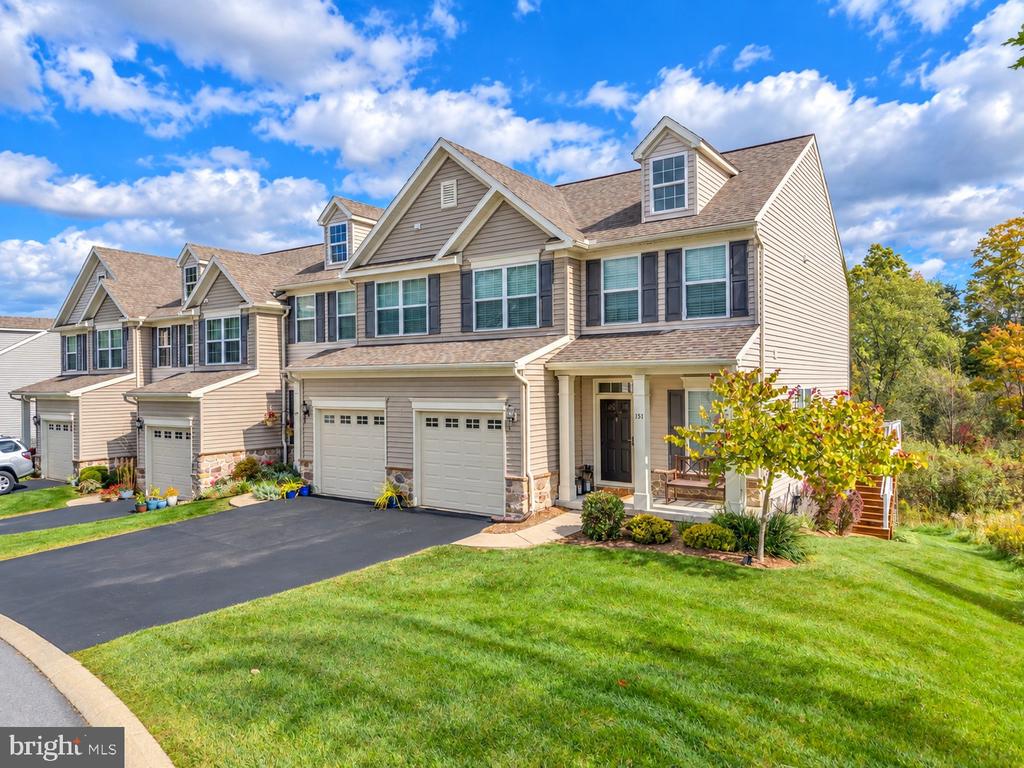 Beige townhouse with a two-car garage, covered porch, and landscaped front lawn.