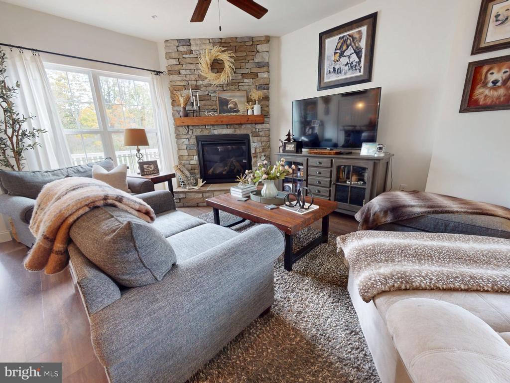 Living room with a stone fireplace, gray sectional, and large curtained windows.
