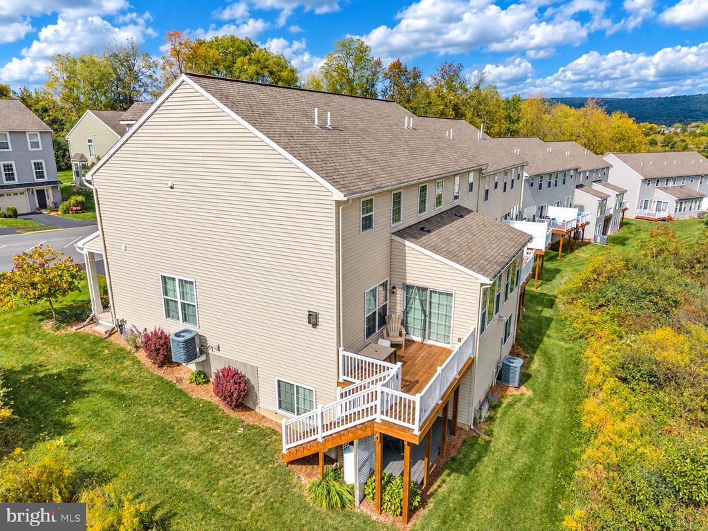 Beige townhome with a raised deck and white railings, viewed from above among attached homes and autumn trees.