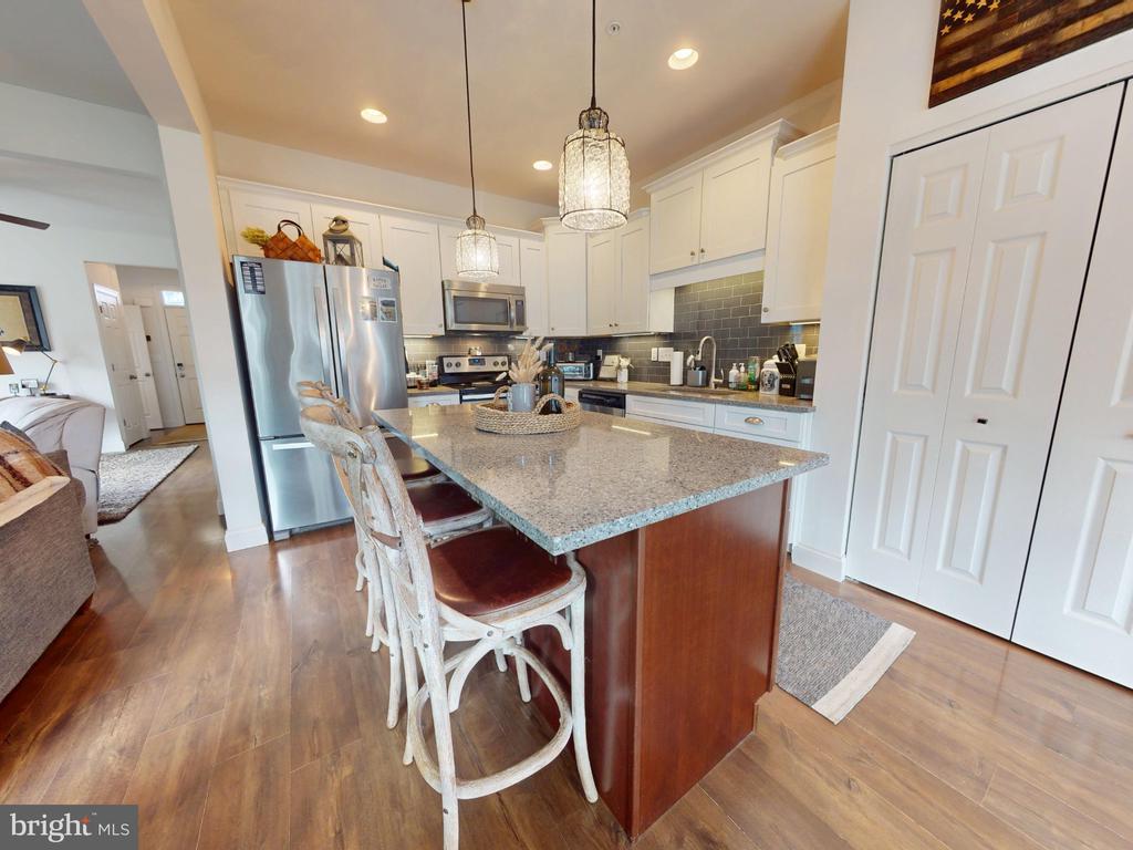 Kitchen with a granite island, stainless steel appliances, white cabinetry, and pendant lights.