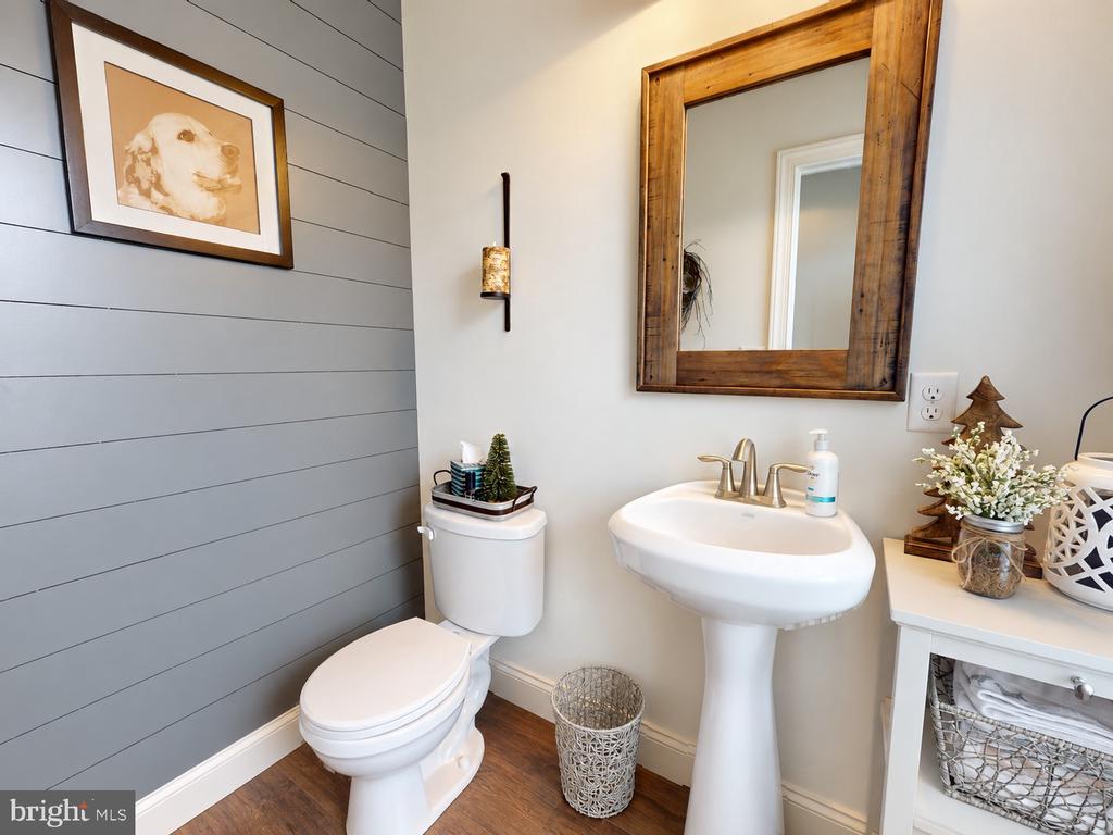 Half bathroom with a pedestal sink, rustic wood-framed mirror, and gray shiplap wall.