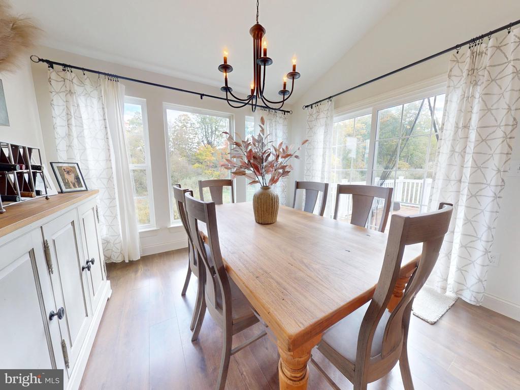 Dining room with a long wood table, dark chandelier, and large windows overlooking trees.