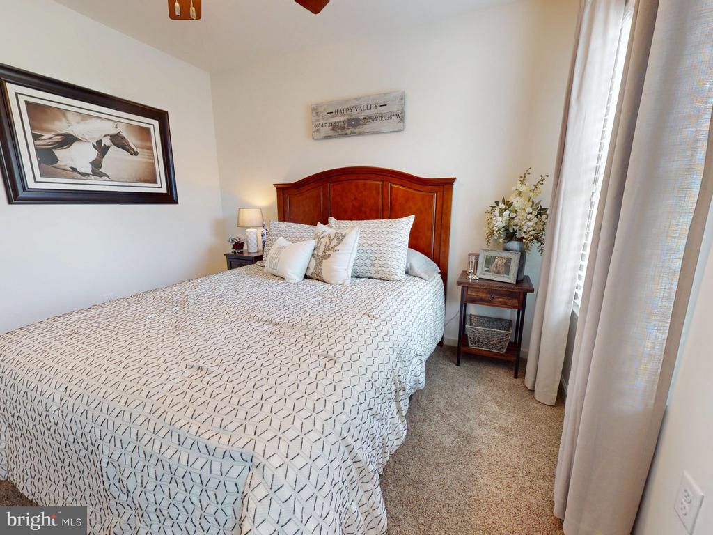 Furnished bedroom with a patterned white bedspread, reddish wood headboard, and tall curtained windows.