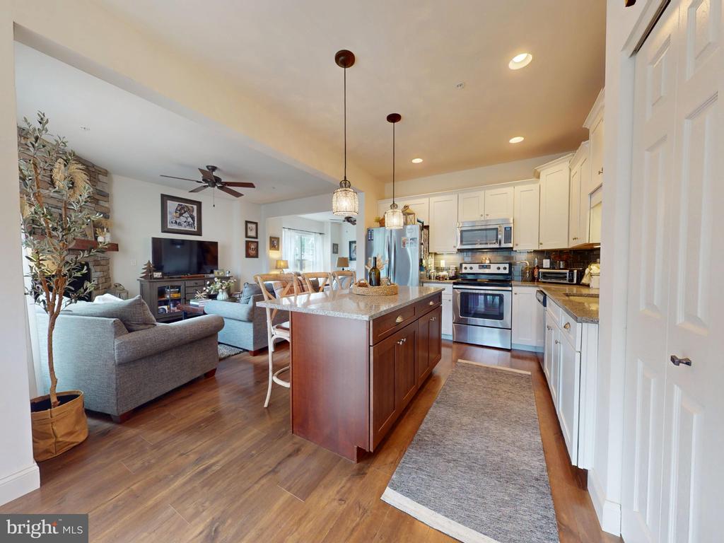 Open-plan kitchen with a dark wood island, white cabinets, stainless steel appliances, and adjoining living area.