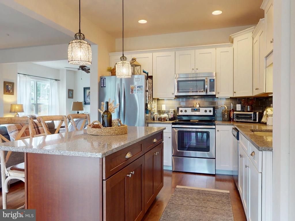 Kitchen with a large dark-wood island, stone countertop, white cabinetry, and stainless steel appliances.