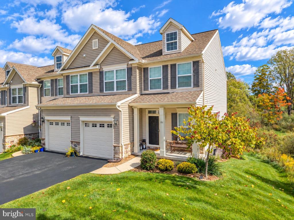 Beige two-story home with two garage doors, a covered porch, and landscaped lawn.