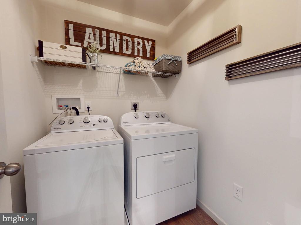 Laundry room with a white washer and dryer beneath wire shelving and a wooden LAUNDRY sign.