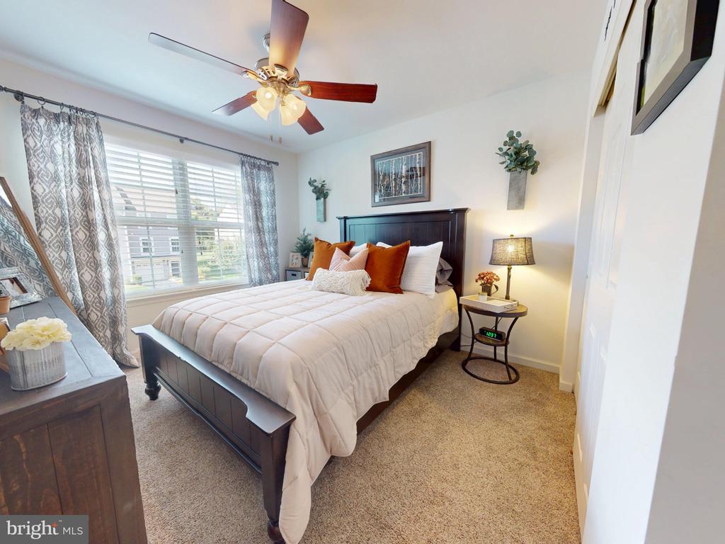 Staged bedroom with a dark wood bed, white bedding, rust-colored pillows, and a large curtained window.