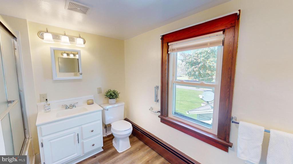 Bathroom with white vanity, toilet, shower enclosure, and a large wood-trimmed window.