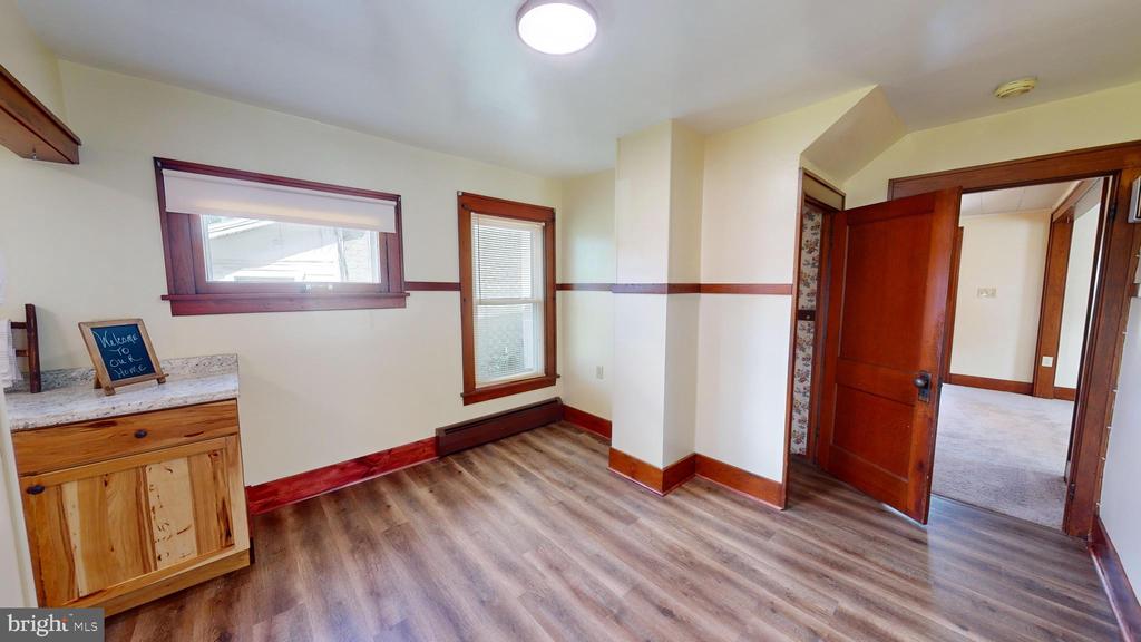 Empty room with wood-look flooring, reddish wood trim, two windows, and an open doorway.
