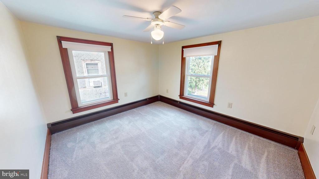 Empty bedroom with two dark-trimmed windows, carpet, baseboard heating, and a ceiling fan.