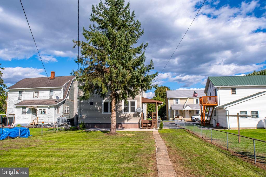 Gray two-story house behind a large evergreen, with a fenced lawn and walkway.
