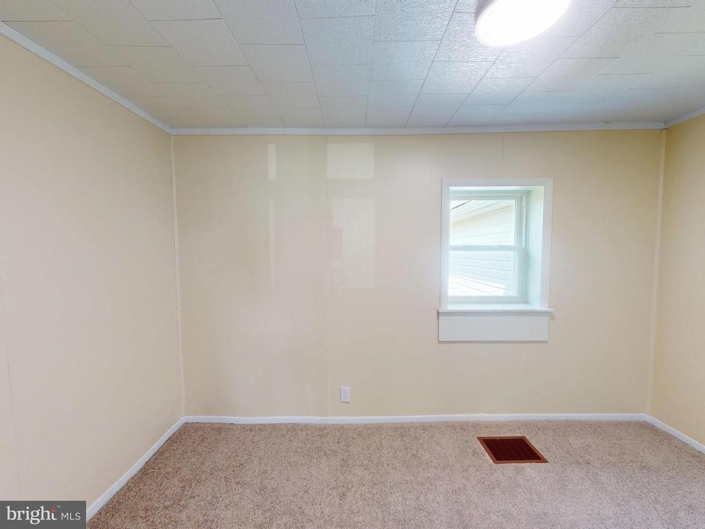 Empty carpeted room with beige walls, a low window, drop ceiling, and floor vent.