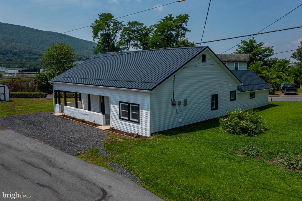 Light-colored home with a dark metal roof, covered porch, and wooded mountain behind it.