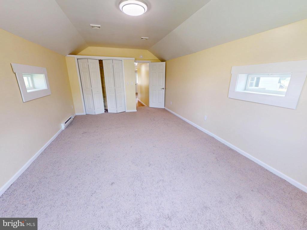 Empty bedroom with light carpet, built-in closets, and a sloped ceiling.