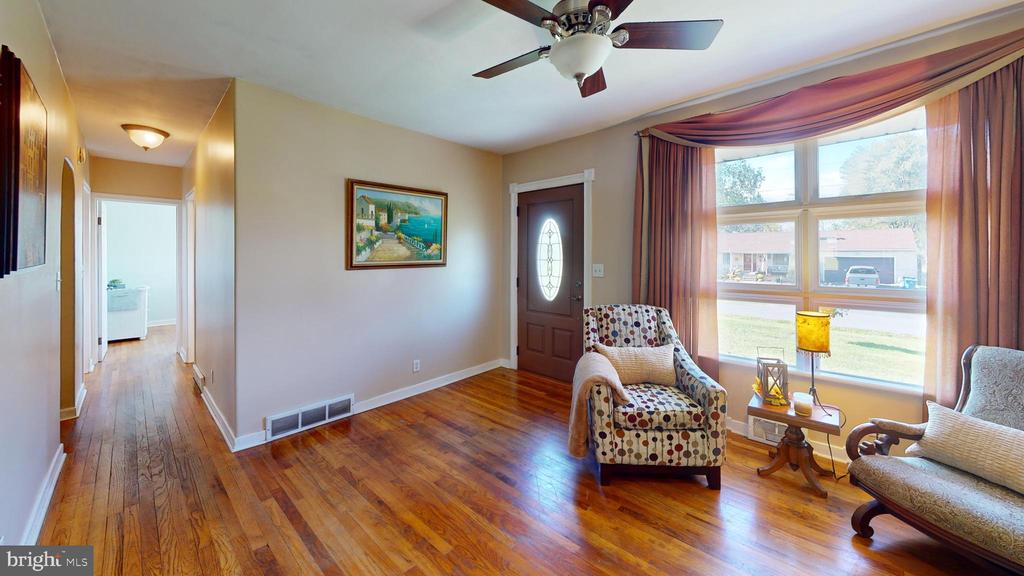 Living room with polished hardwood floors, a ceiling fan, and a large curtained window.