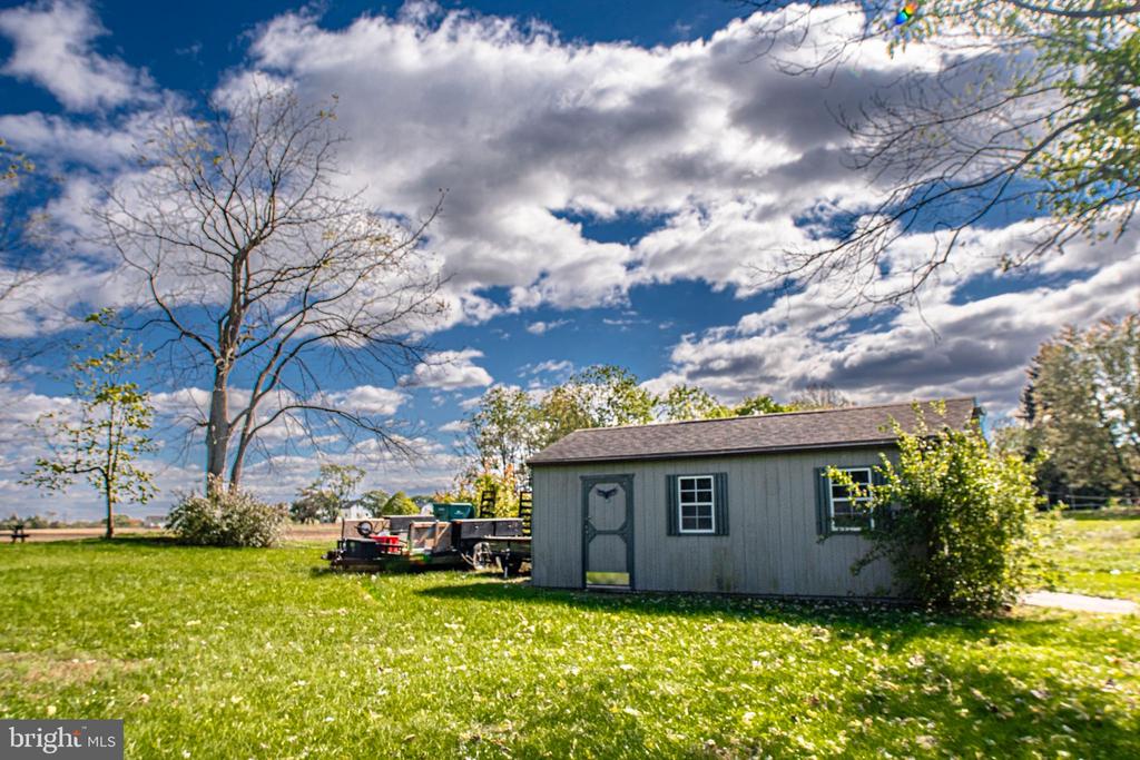 Gray detached shed with two windows in a broad lawn beneath a partly cloudy sky.