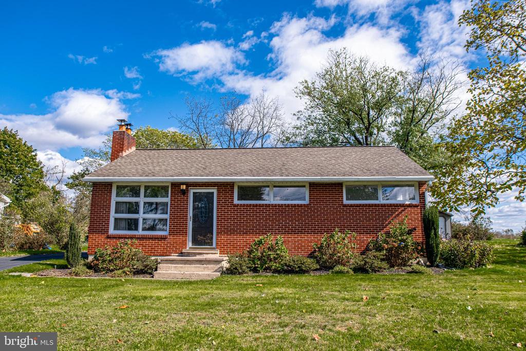 Single-story red brick house with a gray roof, front steps, and a broad lawn.