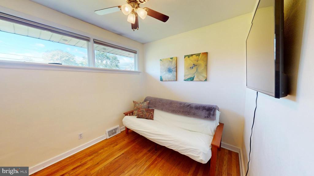 Furnished room with a white-covered futon, hardwood floors, and high windows.
