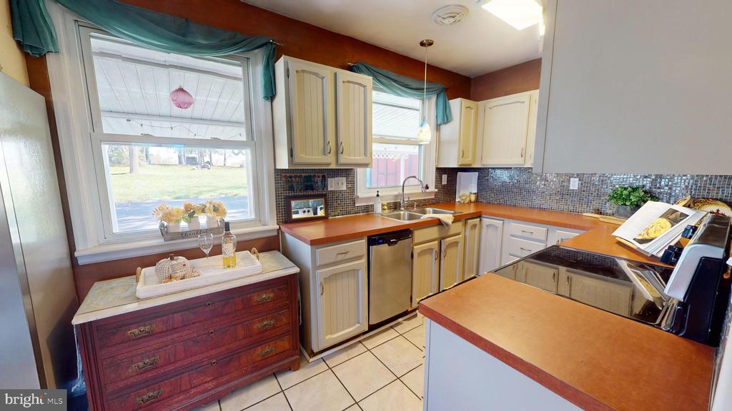 Kitchen with cream cabinets, colorful tile backsplash, and a peninsula cooktop.