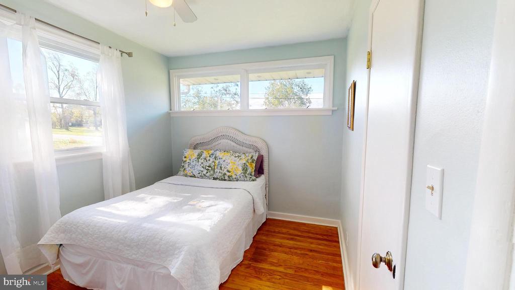 Small bedroom with a single bed, floral pillows, hardwood floors, and several bright windows.