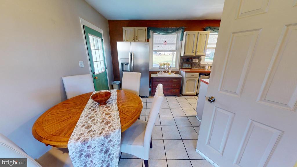 Dining area with a round wooden table beside a kitchen with stainless-steel appliances and light wood cabinets.