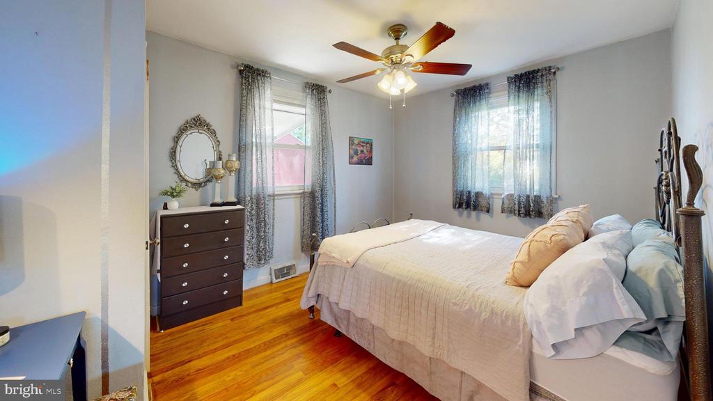 Bedroom with a large light-covered bed, hardwood floors, and two curtained windows.