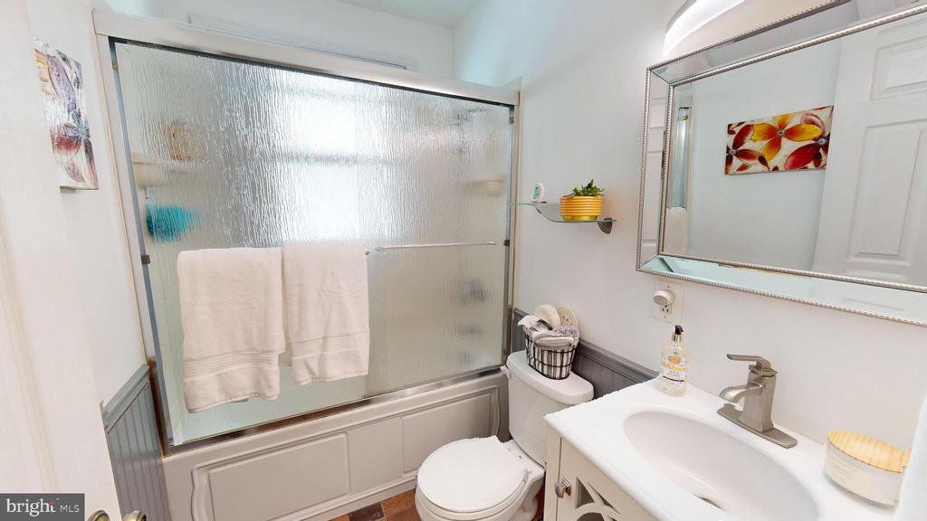 Bathroom with a frosted-glass tub and shower, white vanity, and large framed mirror.