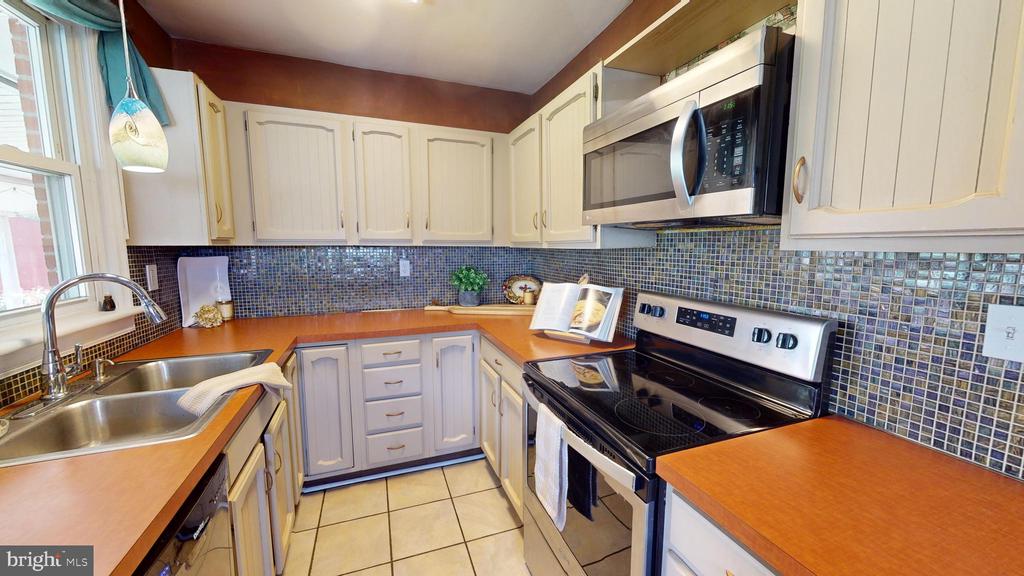 Kitchen with cream cabinets, orange countertops, blue mosaic backsplash, and stainless steel appliances.
