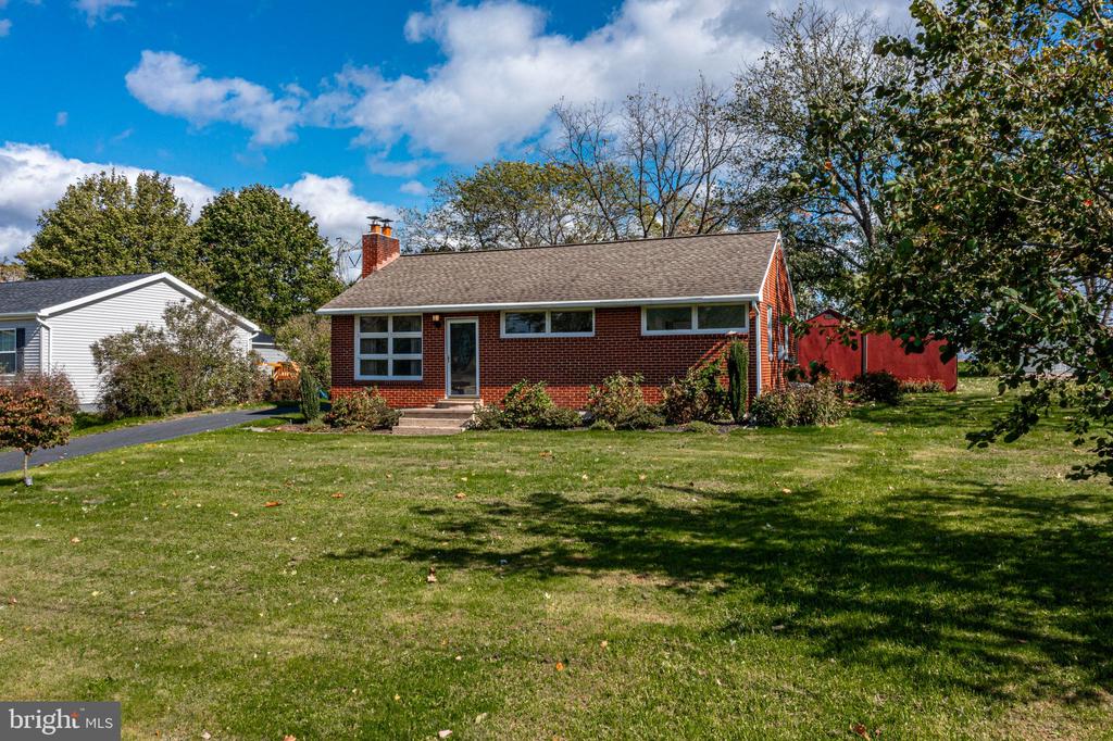 Single-story brick house with front lawn, mature trees, and a red fence.