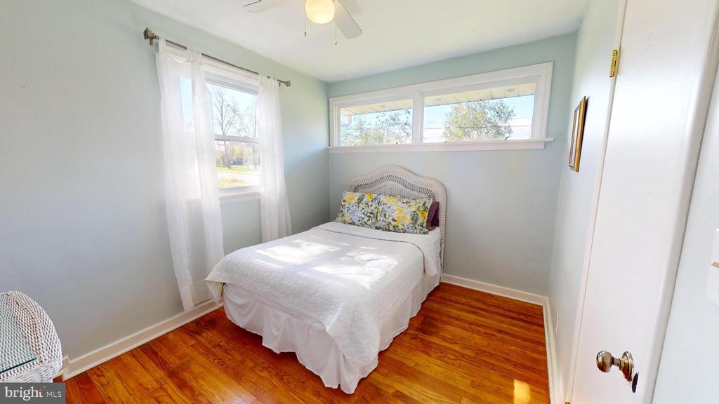 Bedroom with a white bed, floral accent pillow, hardwood floors, and windows on two walls.