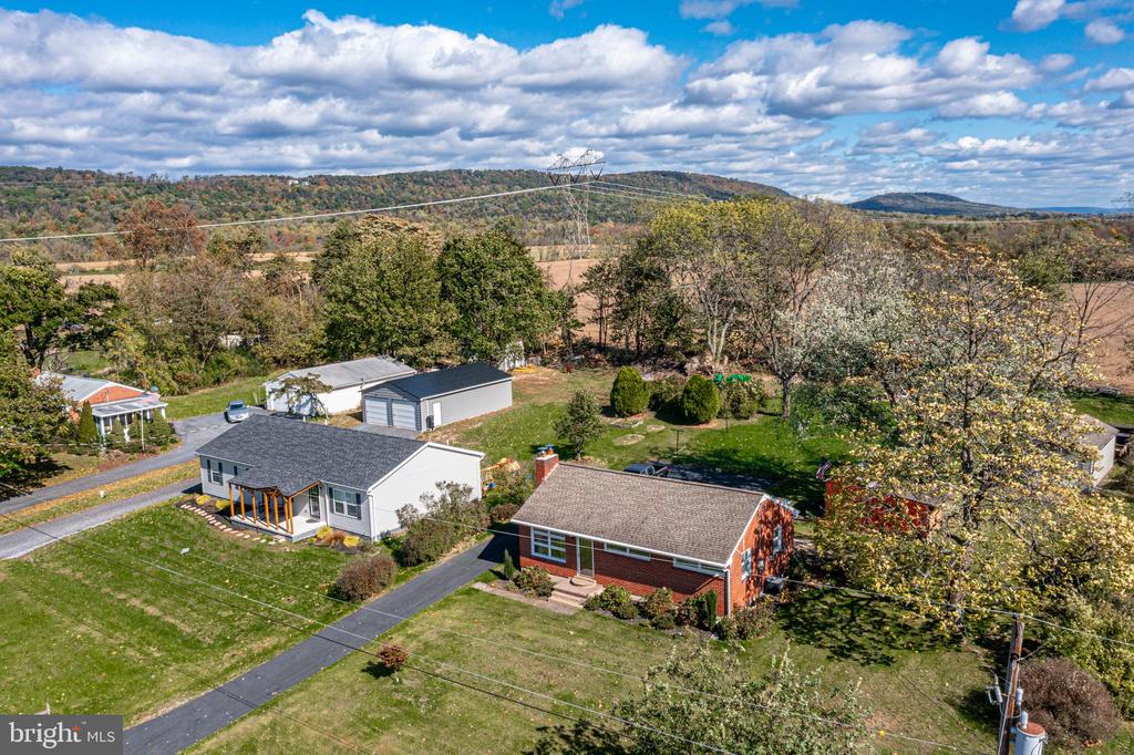 Aerial view of homes amid lawns and autumn trees, with wooded hills in the distance.