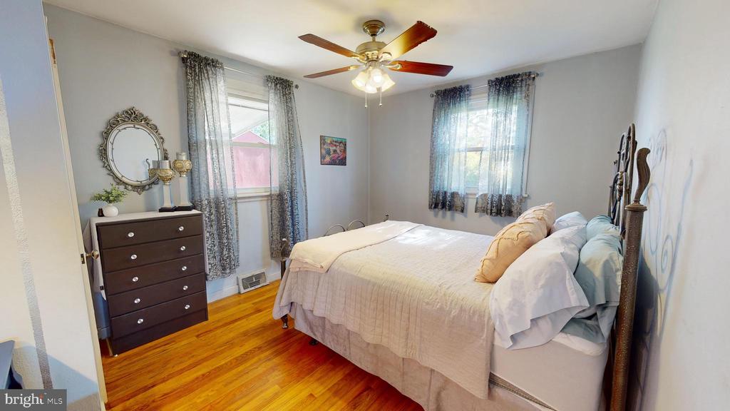 Bedroom with a large bed, hardwood floors, two curtained windows, and a ceiling fan.