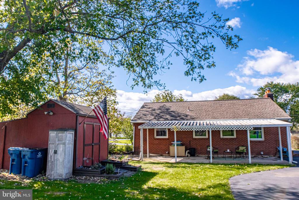 Brick ranch house with a covered patio and red storage shed in the backyard.