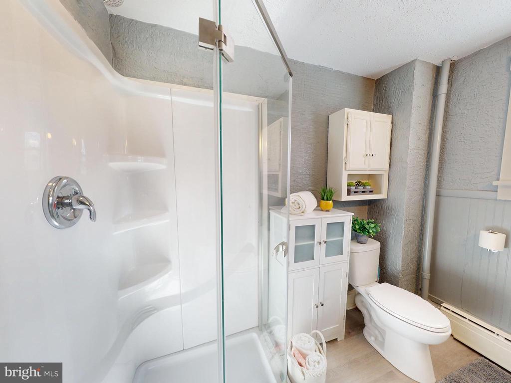 Bathroom with a glass-enclosed shower, built-in shelves, and white storage cabinets beside the toilet.