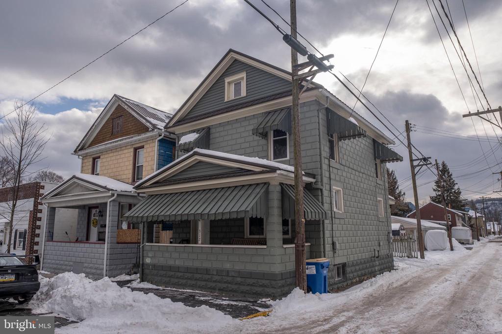 Gray two-story house with a covered porch and striped awnings on a snowy street.