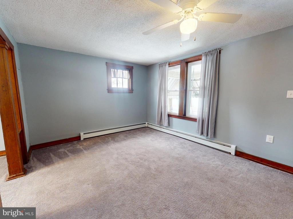 Empty carpeted room with blue-gray walls, wood trim, curtained windows, and a ceiling fan.