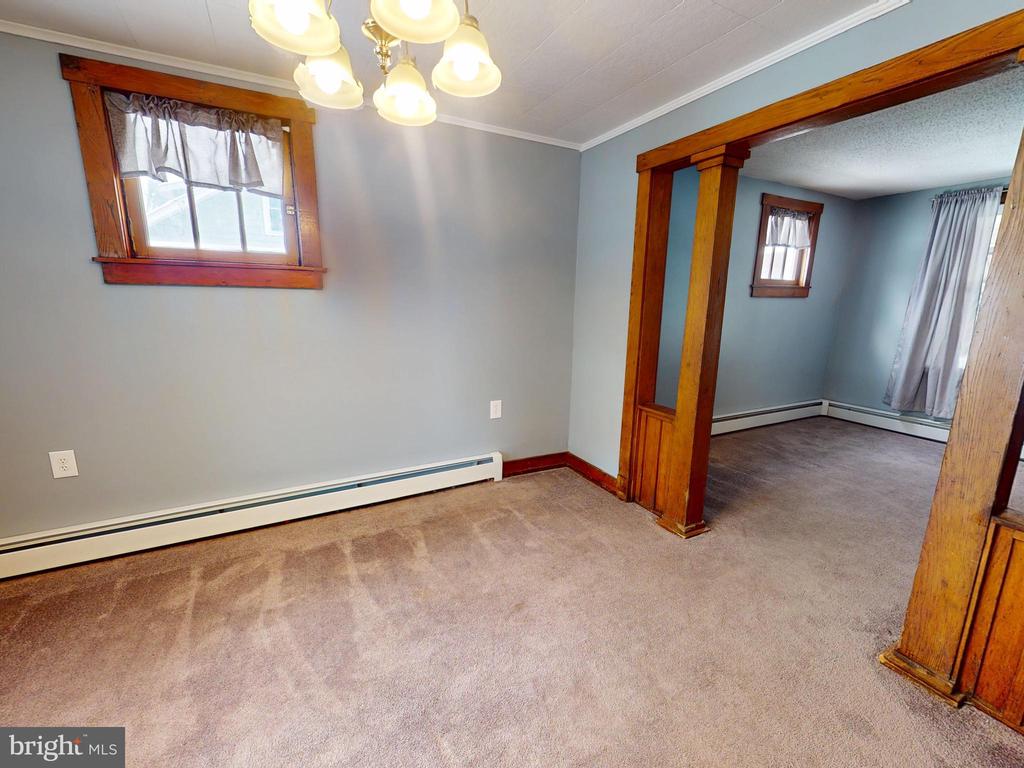 Carpeted room with a ceiling light, wood-trimmed opening, and adjoining empty room.