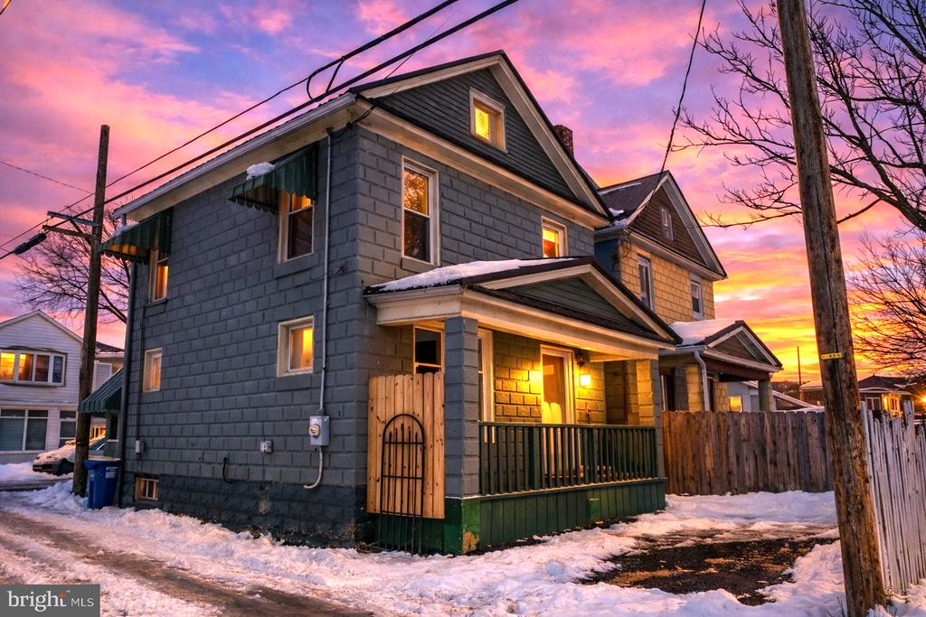 Gray two-story house with a covered porch and snow-covered yard at sunset.