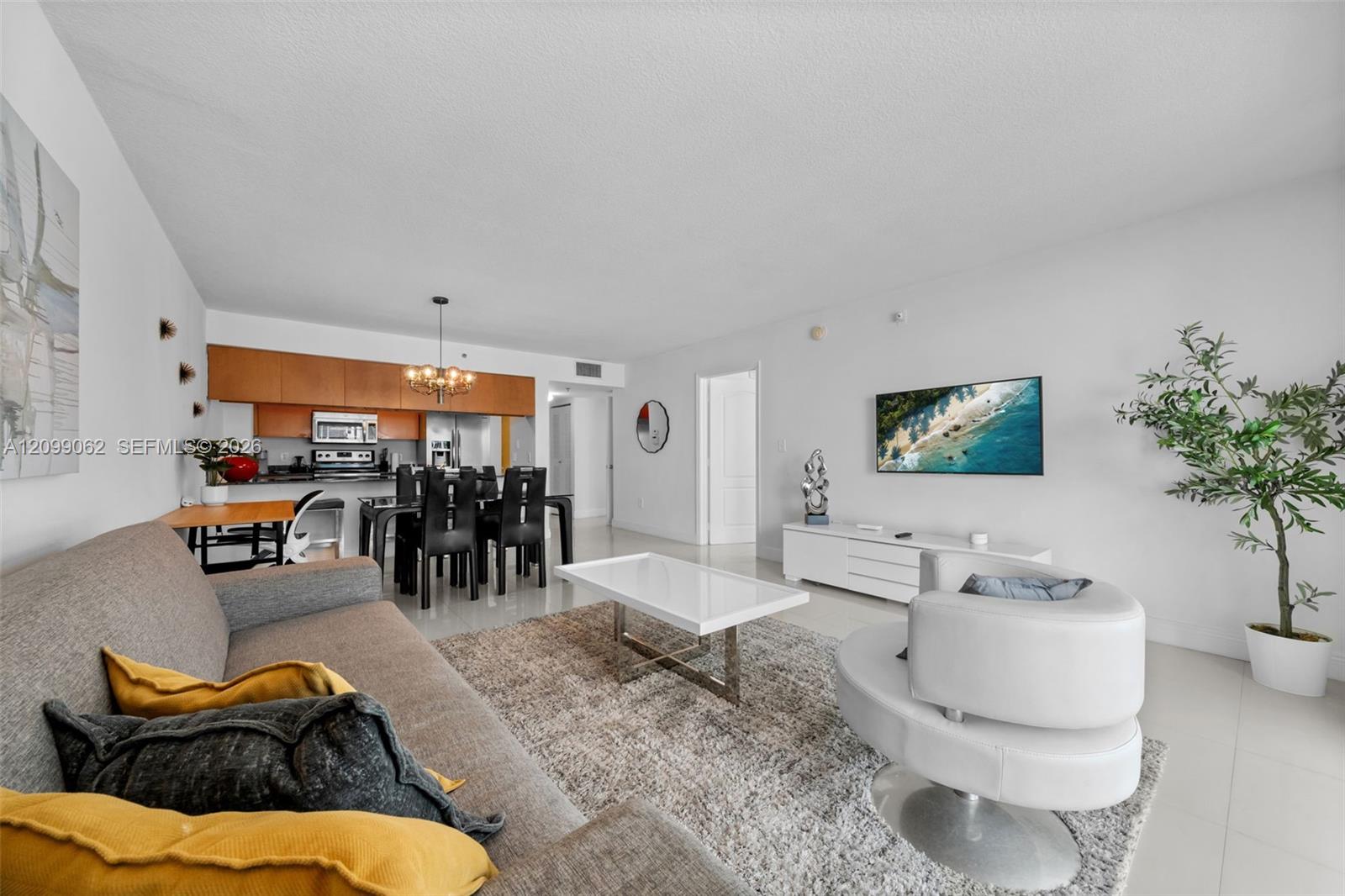 Open-plan condo living room with a gray sectional, yellow pillows, and a white swivel chair.