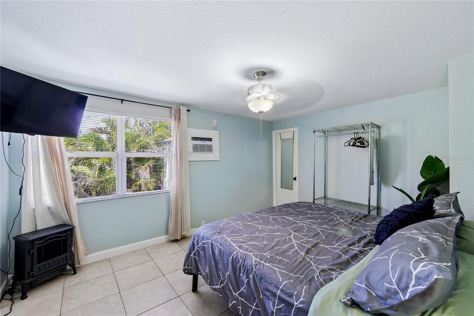 Bedroom with a patterned bedspread, tiled floor, and window overlooking palm trees.