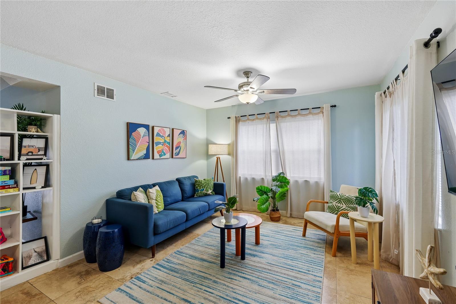 Living room with a blue sofa, tropical plants, and a blue-striped rug.