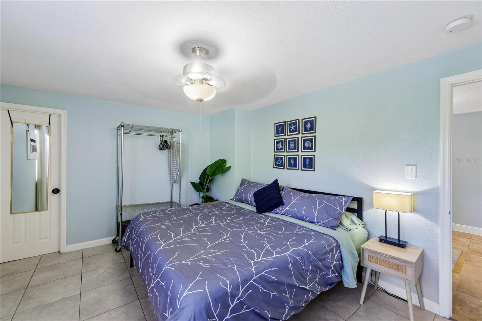 Bedroom with purple patterned bedding, pale blue walls, and gray tile flooring.