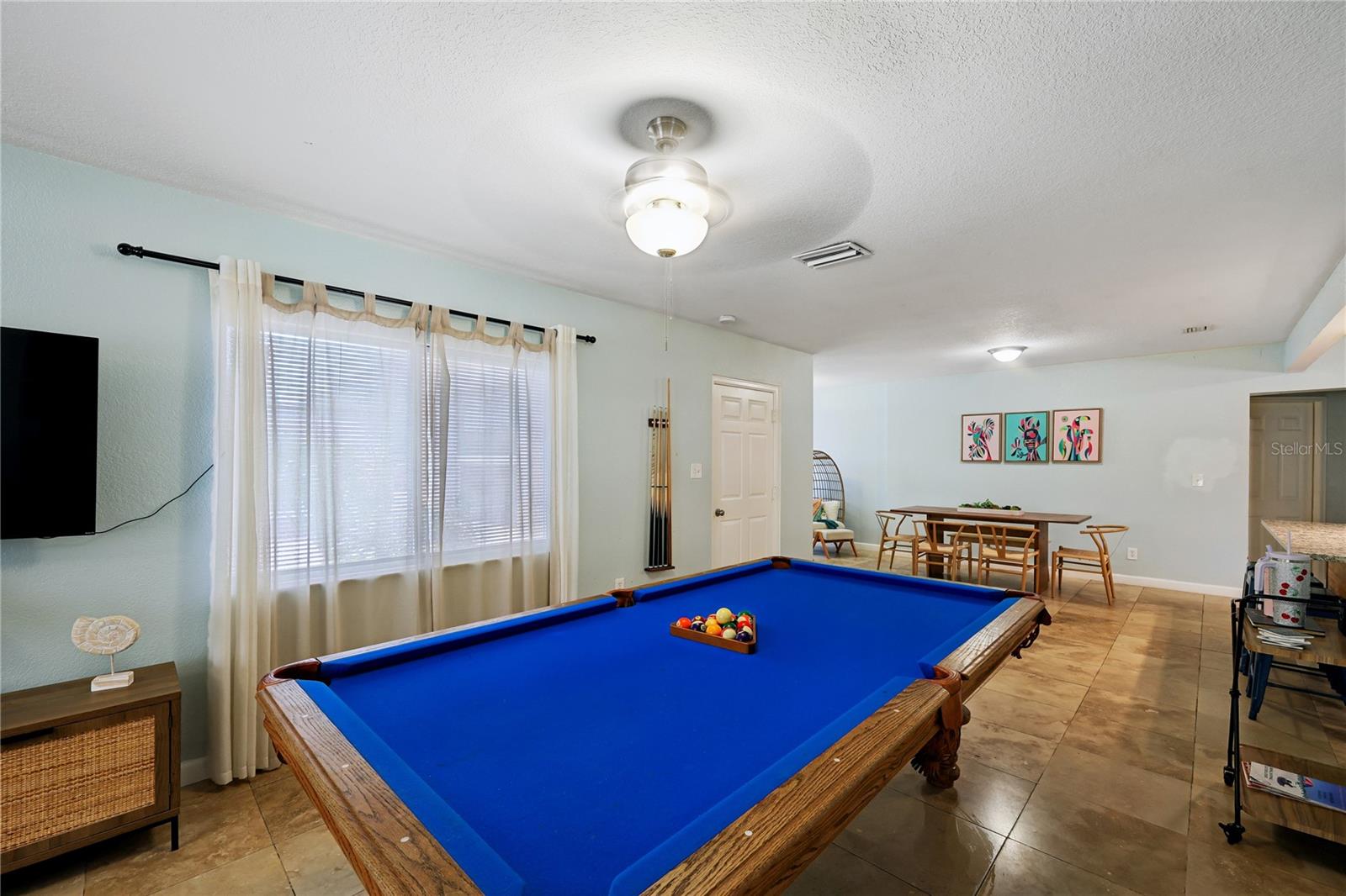 Game room with a blue-felt pool table and a dining area in the background.