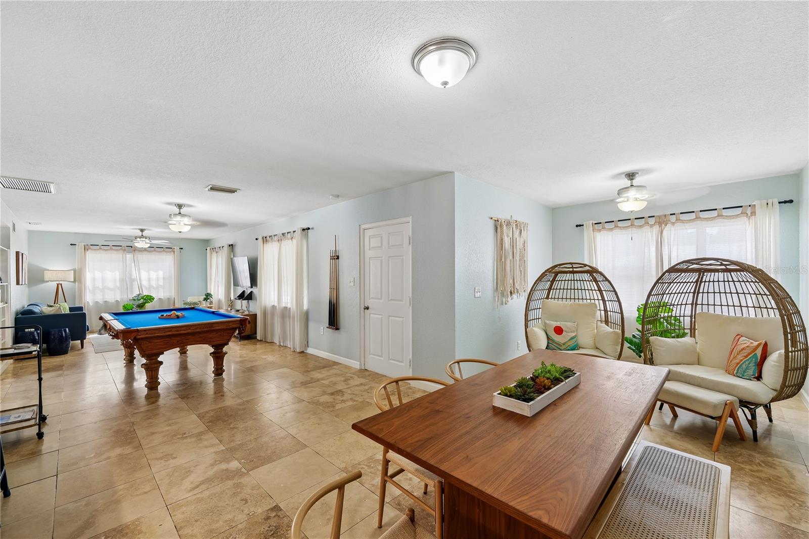 Open living and dining area with a pool table, wicker lounge chairs, and tiled floors.