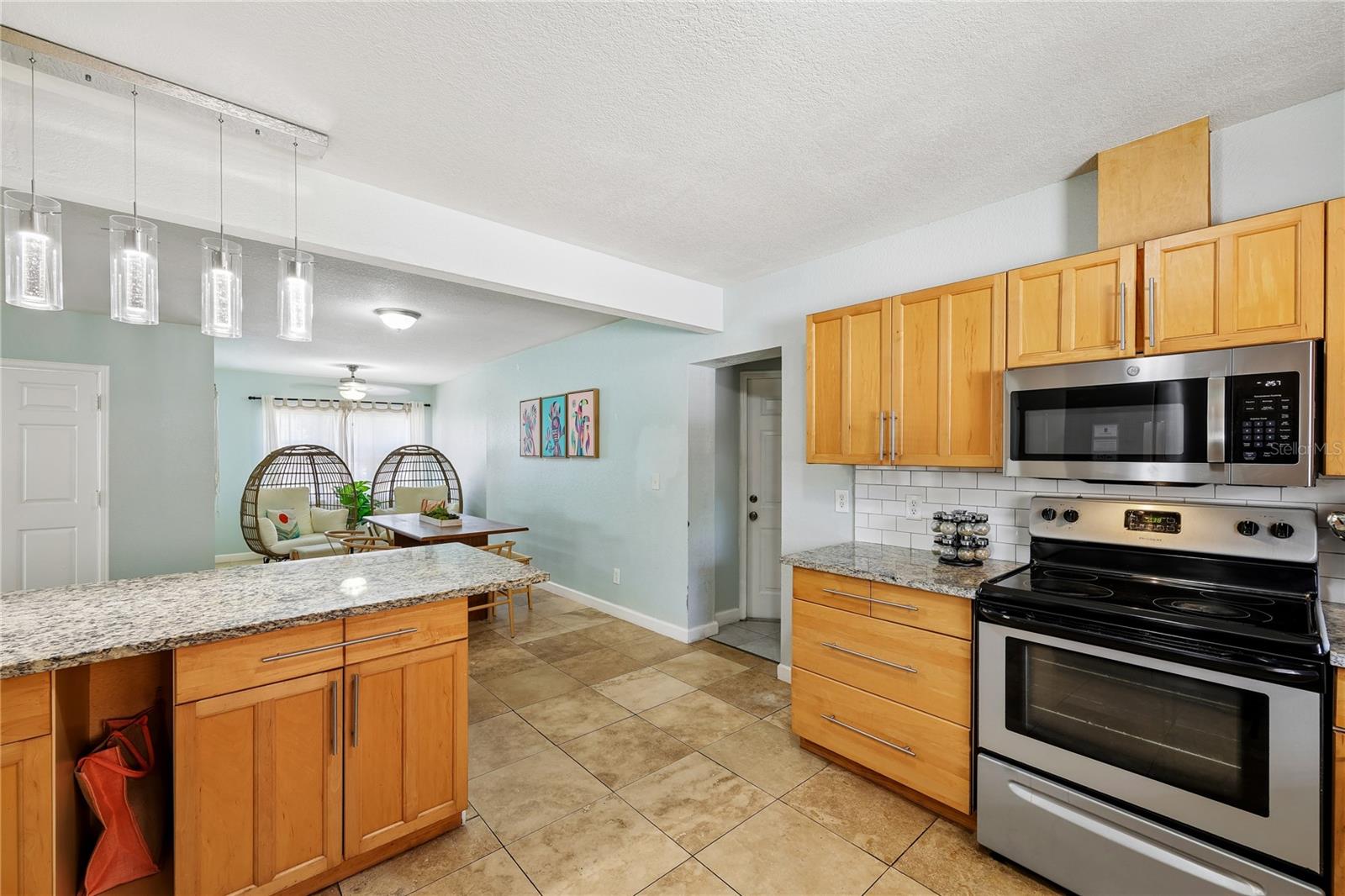 Kitchen with granite counters and wood cabinets opening to a sitting area with hanging egg chairs.